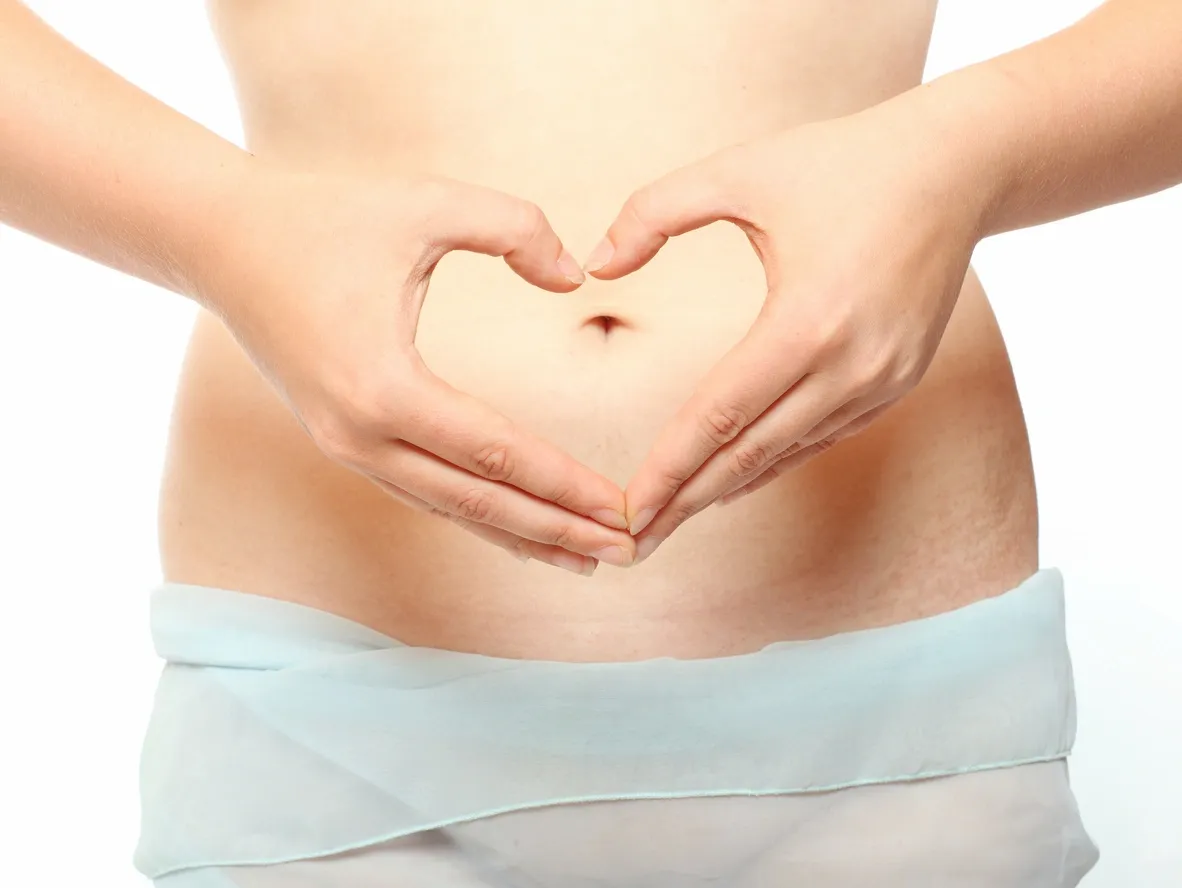 Hands forming a heart shape over stomach — a symbol of body love and healing